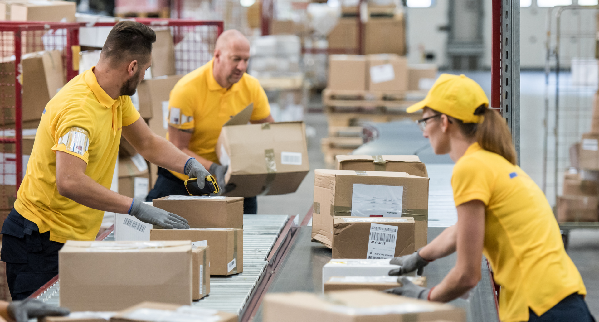 Warehouse staff sorting cardboard boxes on a conveyor belt in a fulfilment centre.